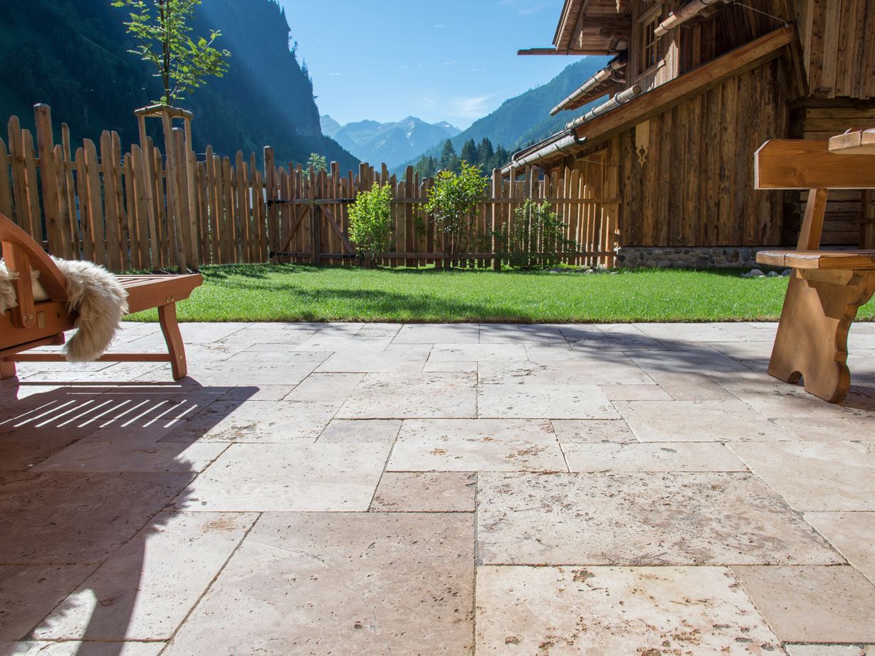 Terrazza con pavimento in travertino Rustic e mobili in legno, sullo sfondo un prato e una vista sulle montagne