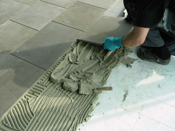 L'installatore posa una Piastrella nel letto spesso su una lastra di cemento.