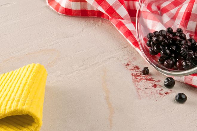 Un panno giallo, un canovaccio rosso e una ciotola di vetro con bacche rovesciata su una pietra naturale.