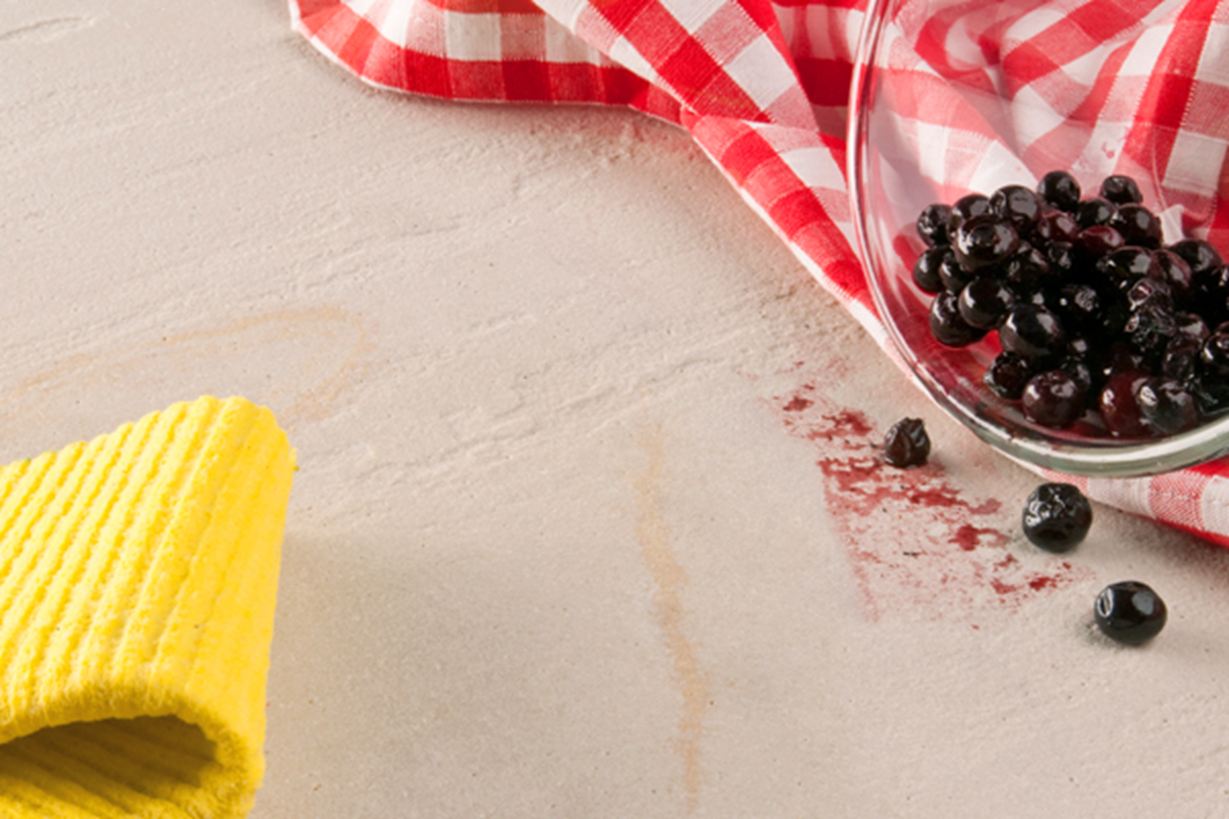 Un panno giallo, un canovaccio rosso e una ciotola di vetro con bacche rovesciata su una pietra naturale.