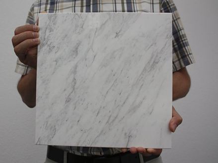 Persona che tiene in mano una piastrella di marmo bianco con venature grigie nella telecamera