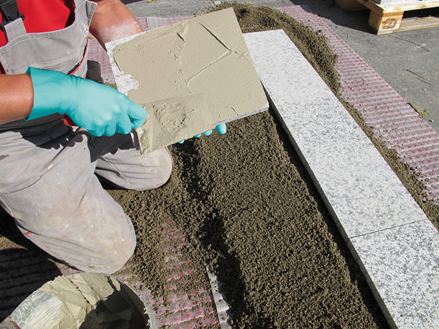 L'installatore riveste il retro della pietra con il collante per la posa con malta monocellulare su massicciata di base