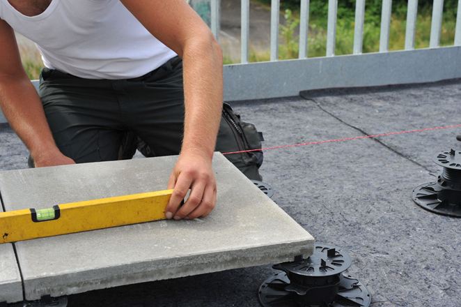 Le lastre vengono posate su piedistalli, l'installatore utilizza una livella a bolla d'aria.