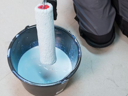 Il piastrellista immerge un rullo in un secchio di primer