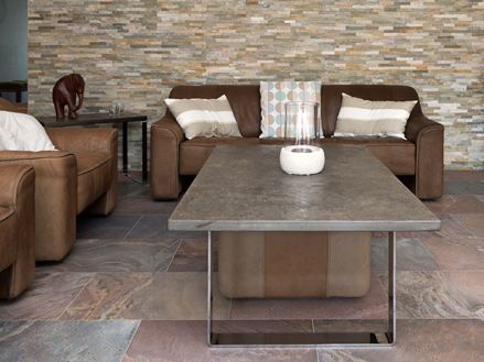 Soggiorno con divano marrone, pavimento in quarzite rossastra e rivestimenti in pietra naturale alle pareti.