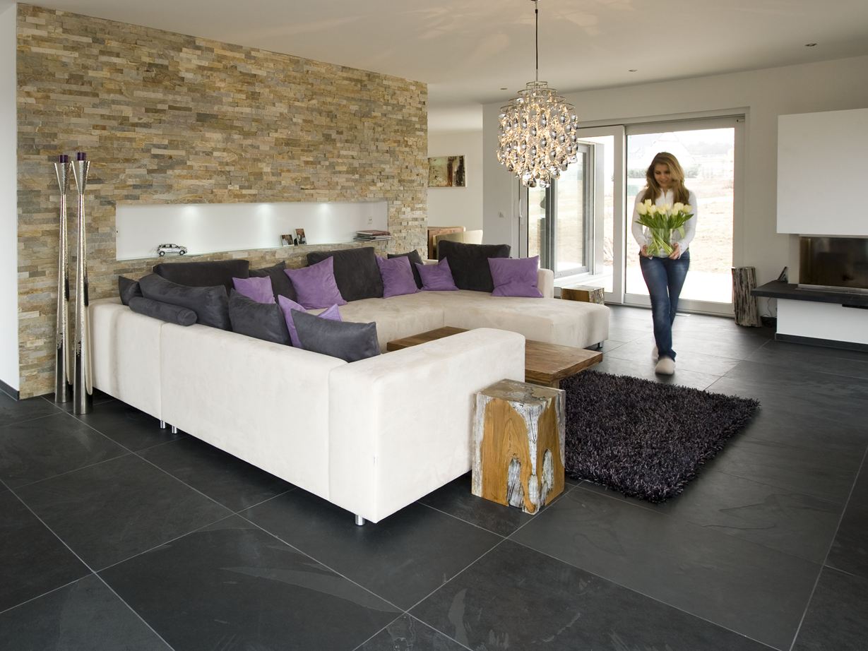 Soggiorno moderno con rivestimenti in pietra naturale alle pareti, pavimento in piastrelle di ardesia e divano bianco