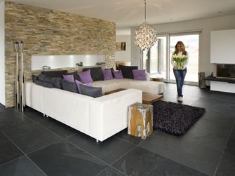 Soggiorno moderno con rivestimenti in pietra naturale alle pareti, pavimento in piastrelle di ardesia e divano bianco